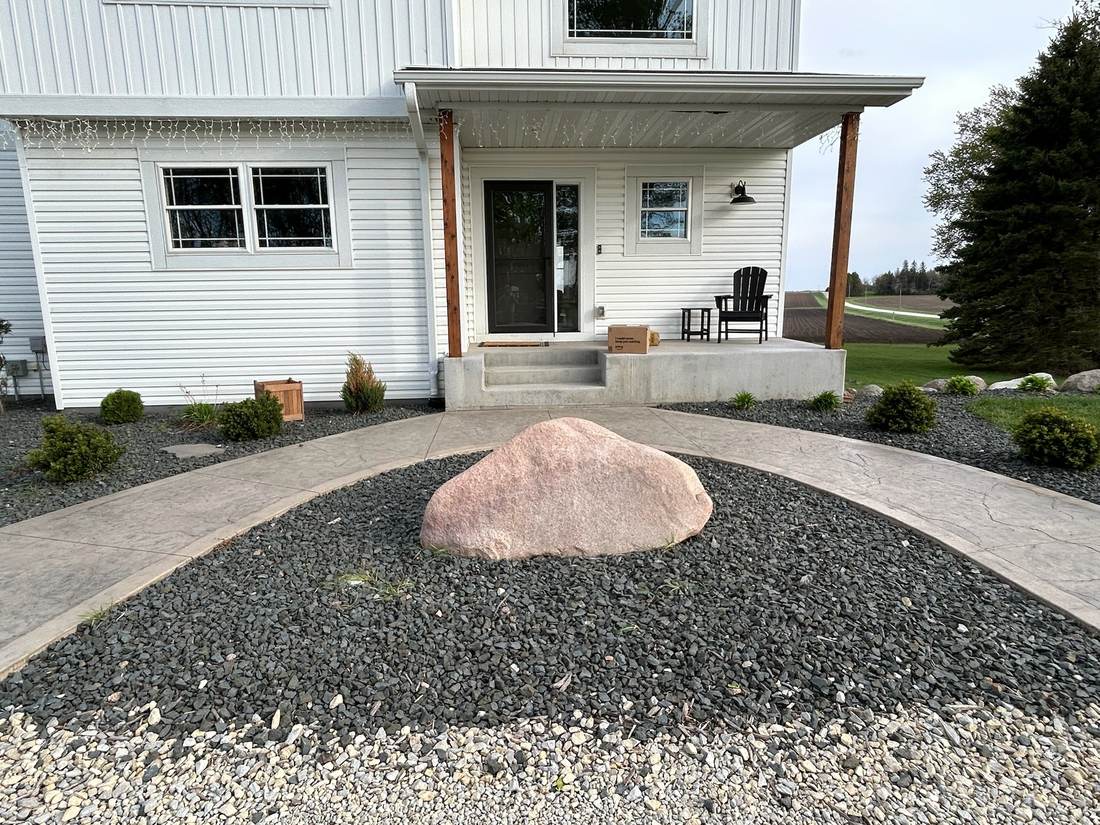 Approximately 5 foot pink boulder set in landscaping rock near an entryway