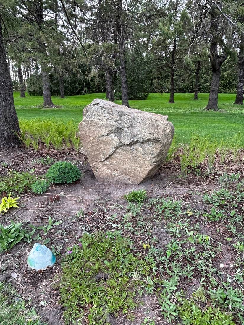 Approximately 5 foot textured boulder set in a wooded lawn