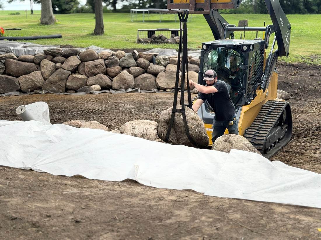 Crew member setting a boulder with the skid steer