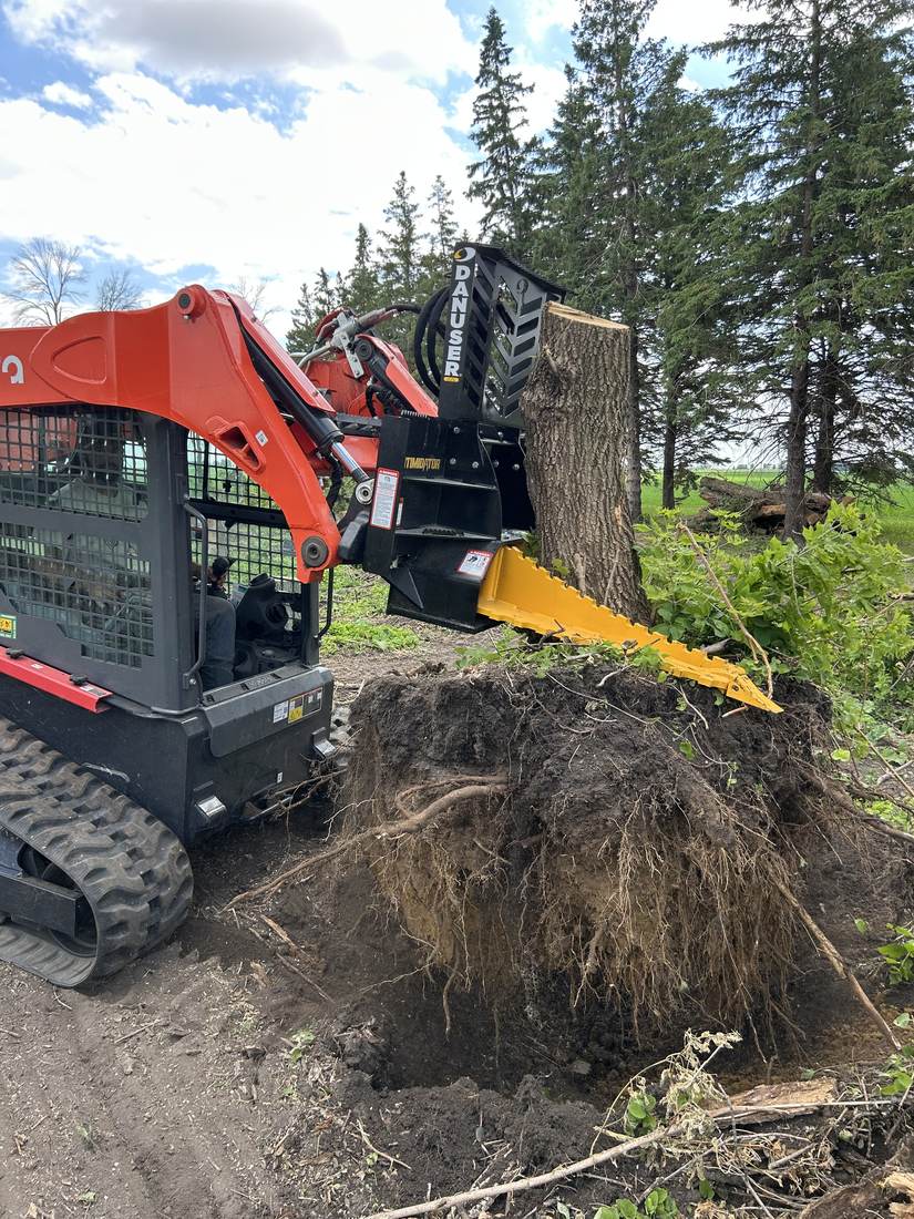 Skid steer with tree removal attachment pulling a stump