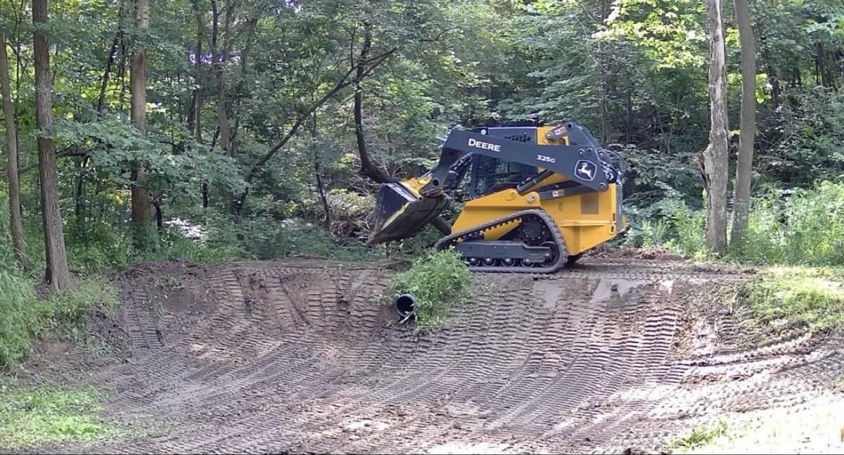 Skid steer grading the slope of a pond basin on a hunting property